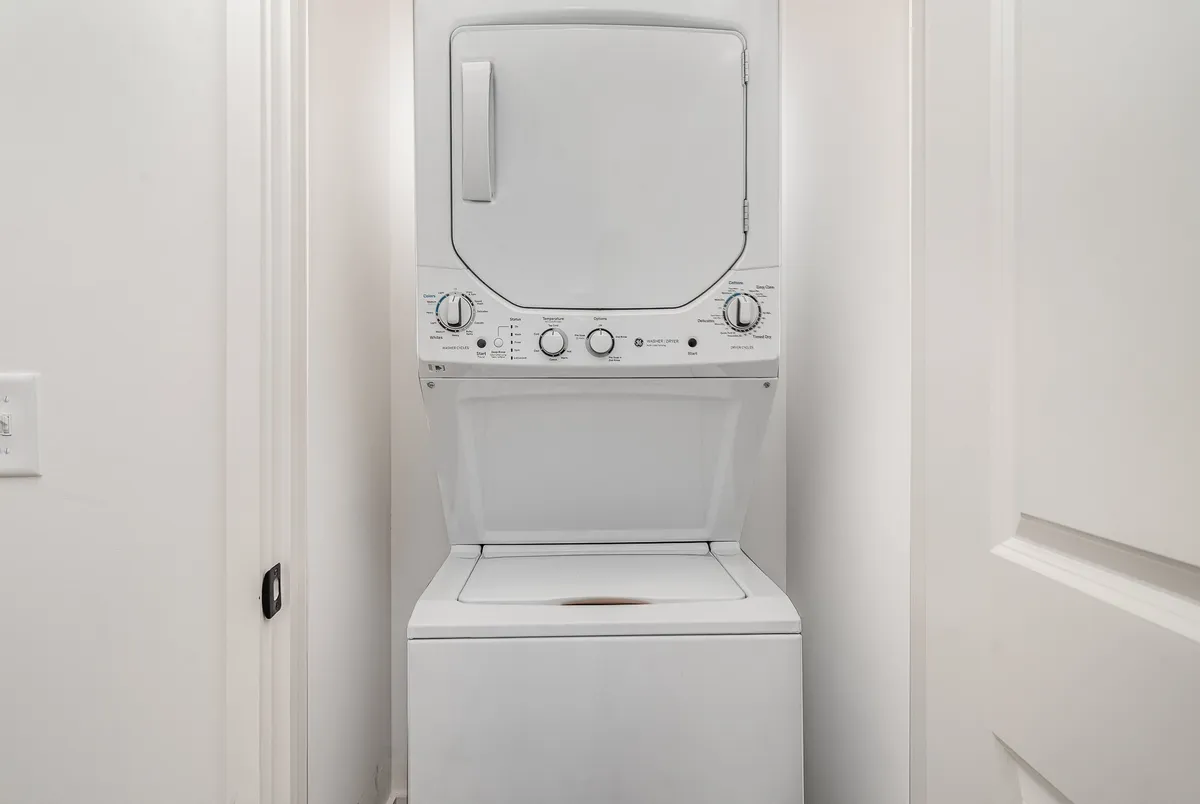 The image displays a modern, stackable washer and dryer set tucked neatly into a dedicated laundry space. The neutral, practical design emphasizes the convenience of in-home laundry, ensuring ease for guests of all ages.