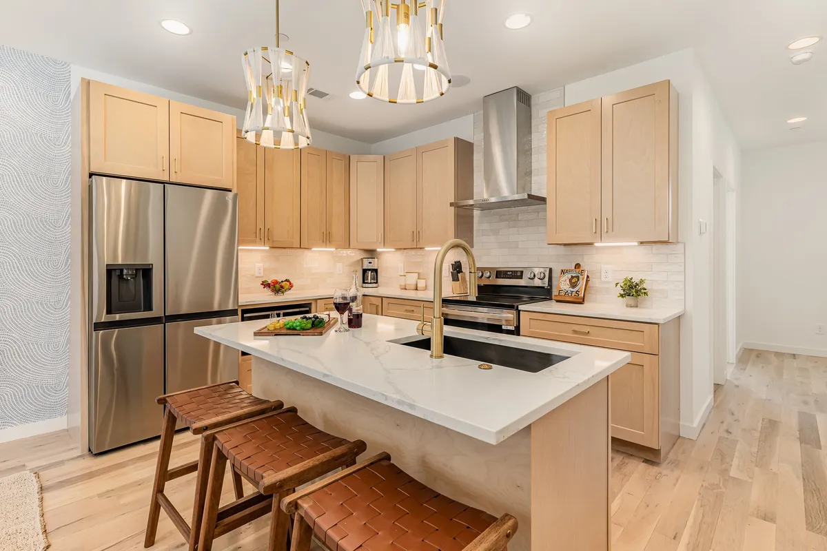 A modern kitchen featuring a central island with bar seating, stainless steel appliances, textured backsplash, and stylish lighting. The layout is open and inviting, ideal for both cooking and entertaining guests.