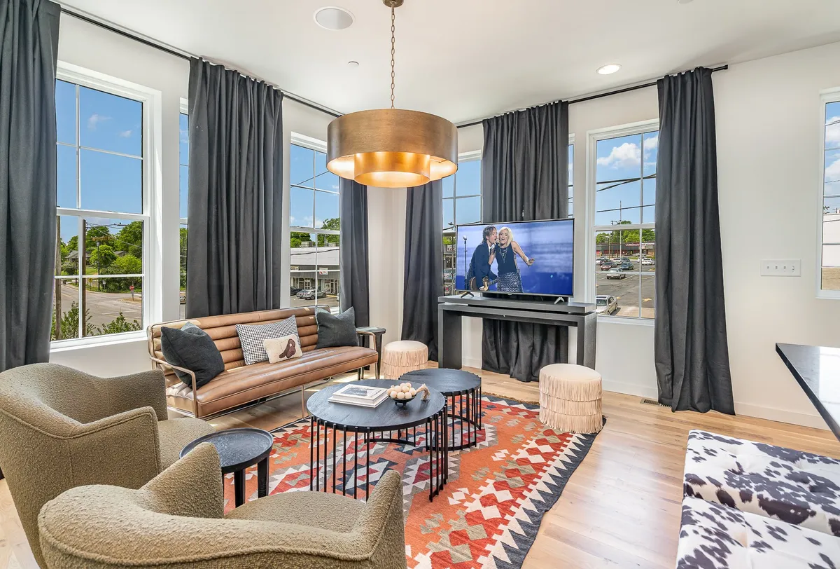 The image showcases a cozy and contemporary living area featuring a large, inviting sofa, a stylish coffee table, modern light fixtures overhead, and a mounted TV. The space exudes warmth and comfort, ideal for relaxing, watching movies, hosting game nights, or gathering with friends and family. The room is bright and welcoming, perfect for large groups to unwind together.