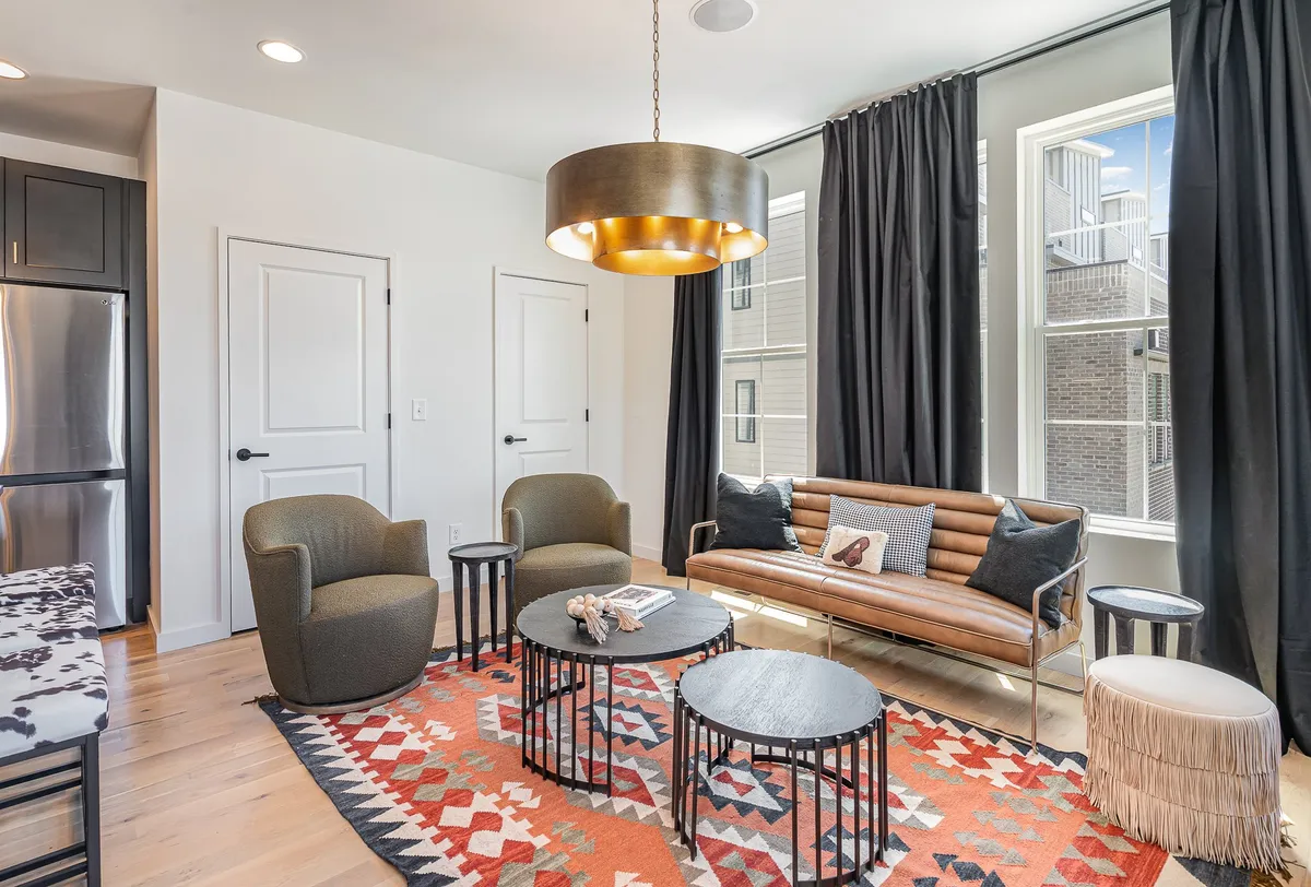 This image shows a cozy second living area featuring a sofa, rug, hanging light, chairs, and coffee tables. The arrangement invites both intimate conversations and relaxed moments for families or groups, capturing the flexible, social nature of the space.