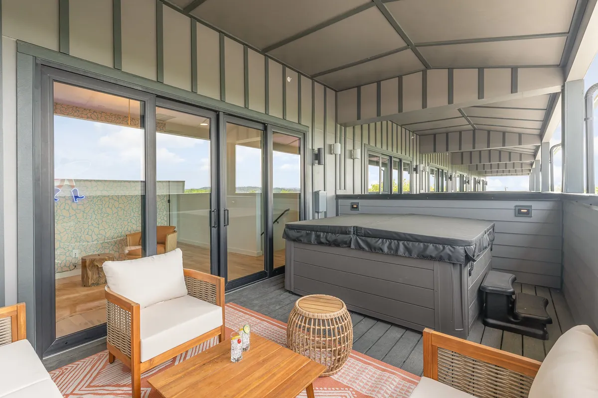 An inviting rooftop scene with a hot tub, plush outdoor seating, a wooden table, and a decorative rug. The arrangement is ideal for groups to gather, with sunset hues and an open-air atmosphere that feels ideal for stargazing and evening conversations.