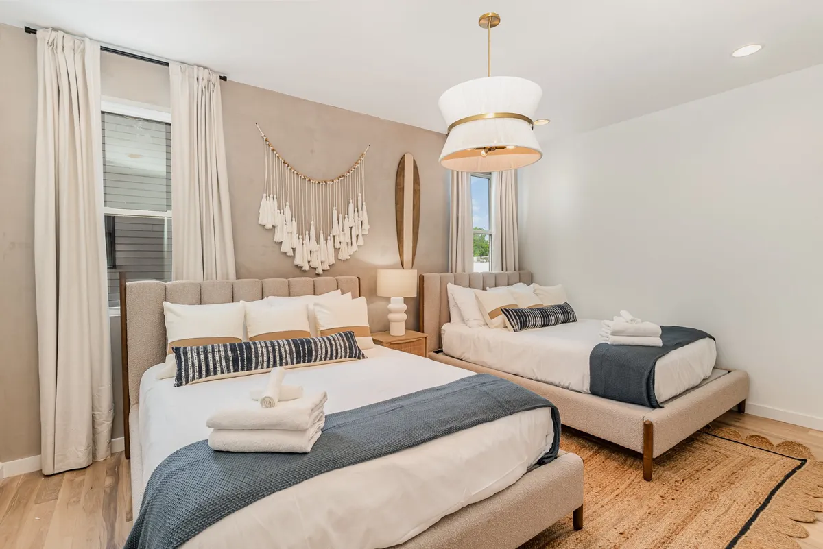 A welcoming room with two beds adorned with decorative pillows, a stylish light fixture, and woven wall decor. The space is bright, flexible, and comfortable—ideal for children, teens, or extra guests, and suited to both relaxation and conversation.