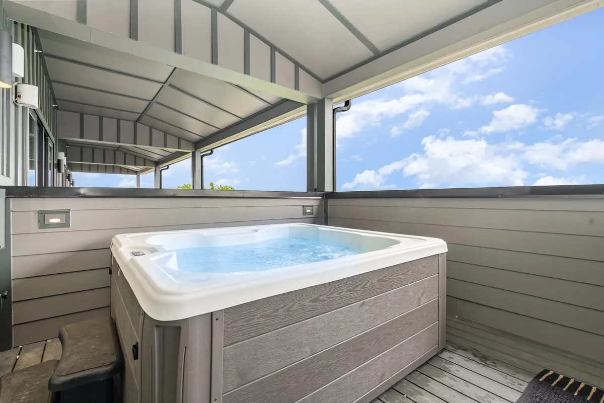 This exterior image features a rooftop hot tub surrounded by a spacious deck, with wide views of the sky hinting at city skyline vistas. The setting is tranquil, with comfortable seating areas that invite relaxation and group socializing as daylight fades.