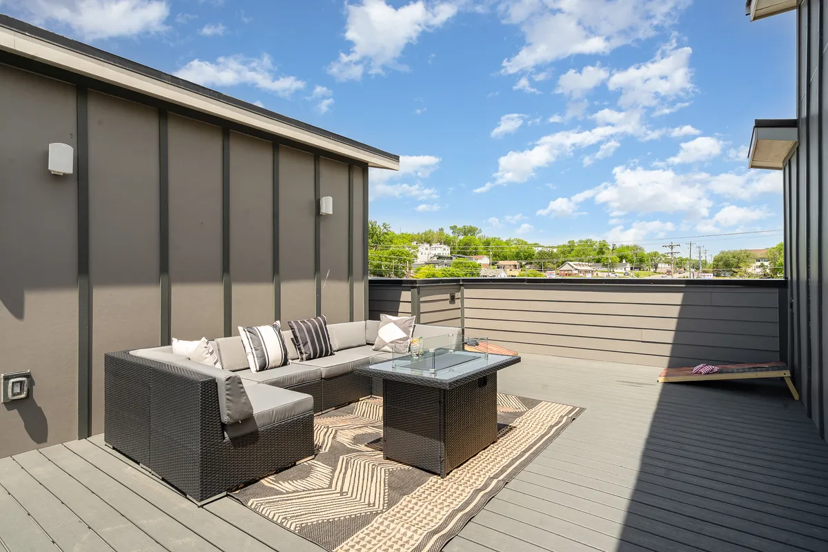 This exterior shot showcases an inviting outdoor seating area with a glass coffee table, decorative rug, and lush greenery. The space is arranged for relaxation or socializing, with plenty of natural light and an open, welcoming atmosphere.