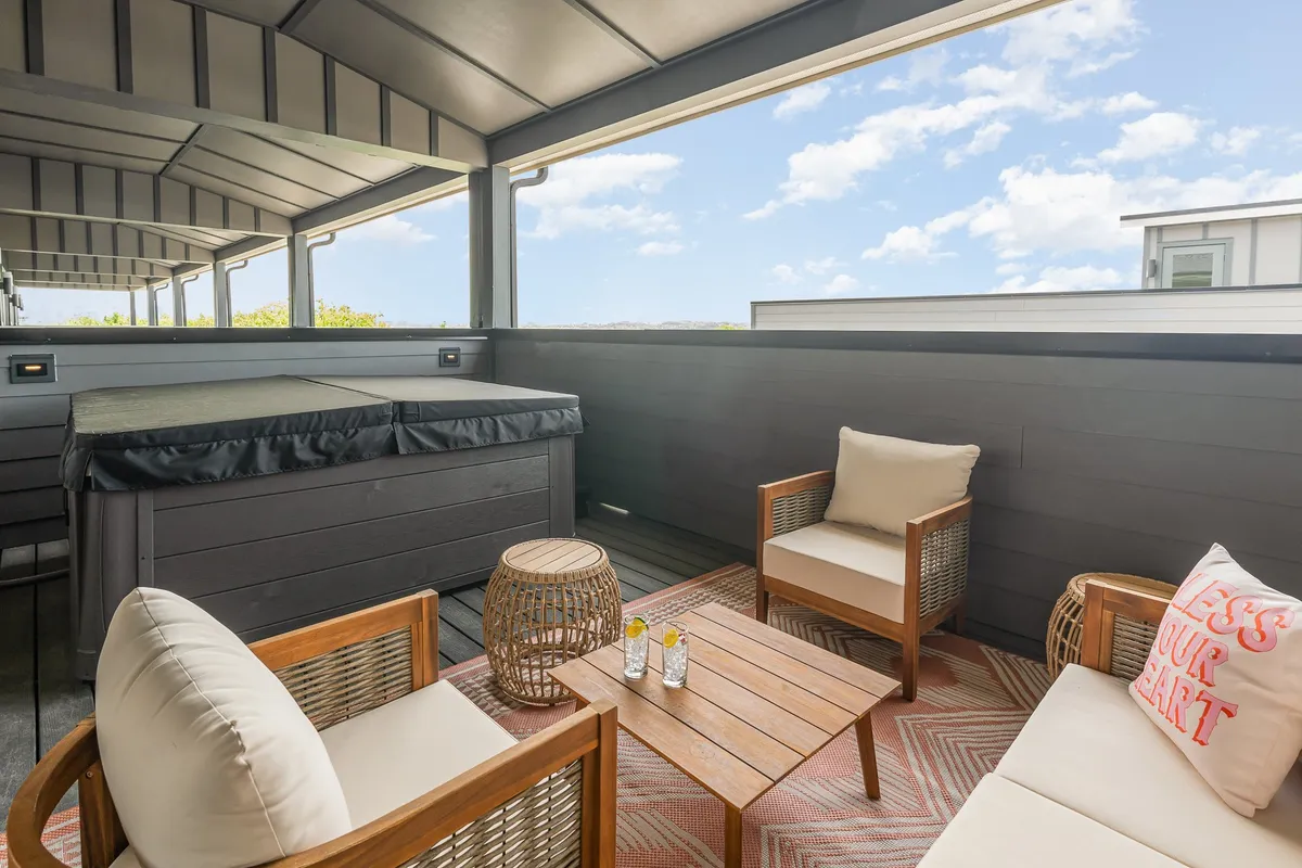 This exterior image features a stylish outdoor patio with a hot tub, comfortable seating, and a textured rug. The scene is set for guests to unwind under the stars, socialize, or enjoy a drink in an inviting atmosphere that captures Nashville’s laid-back, social vibe.