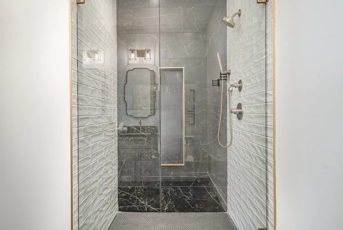 A serene, elegant bathroom with a glass shower enclosure, marble walls, gold accents, and modern fixtures. The space invites relaxation and indulgence in soothing self-care routines.