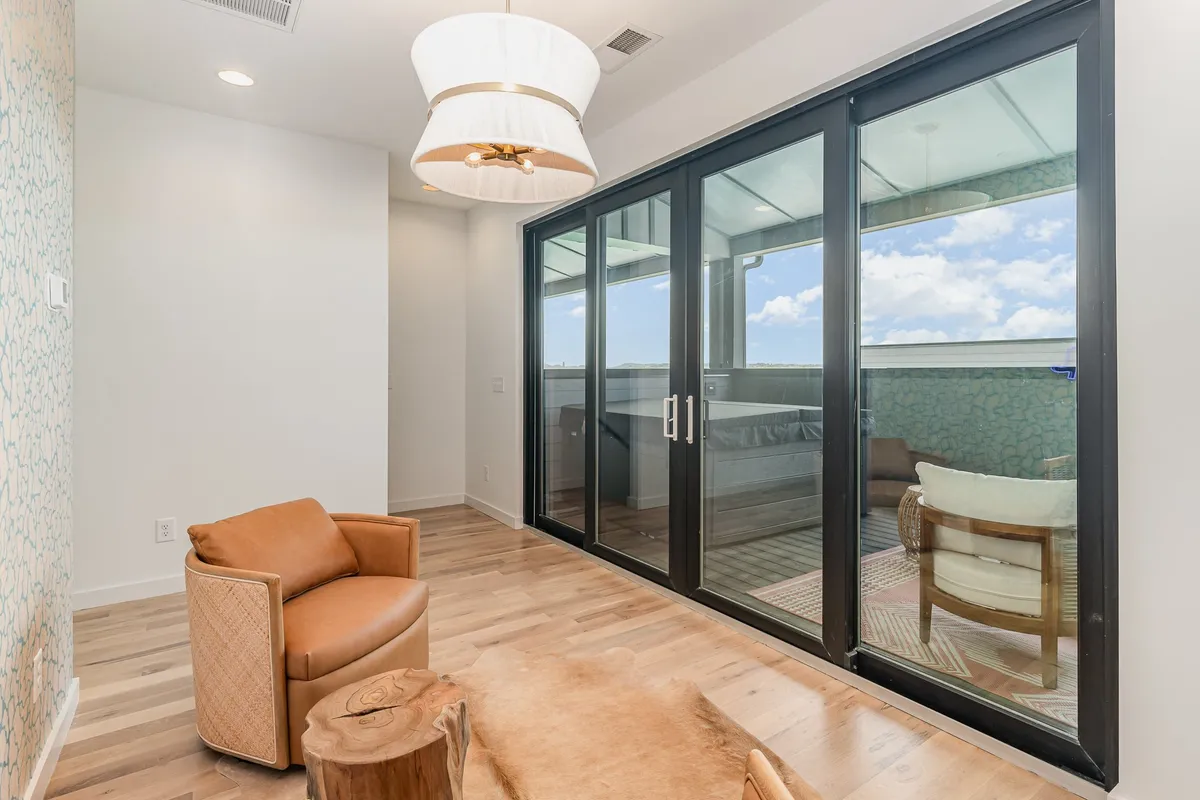 A modern lounge chair is positioned by large glass doors that open to a sweeping view, with soft, natural light streaming into the space. The clean lines, decorative light fixture, and inviting textures create a peaceful setting, while the connection to the outdoors is emphasized by the glass doors.