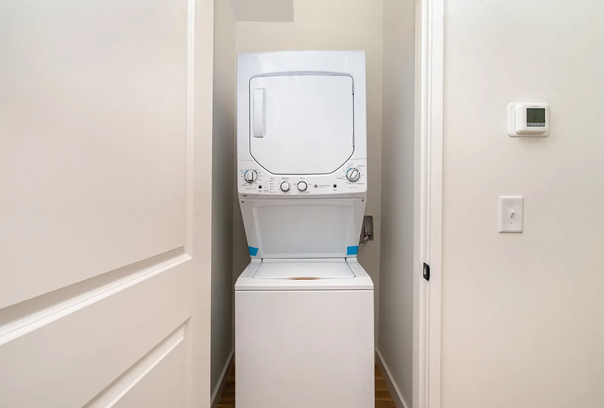 A practical laundry area with stacked washer and dryer, adjacent to a doorway, and a thermostat on the wall. The setup is modern and clean, making it easy for families to keep up with chores during longer stays.