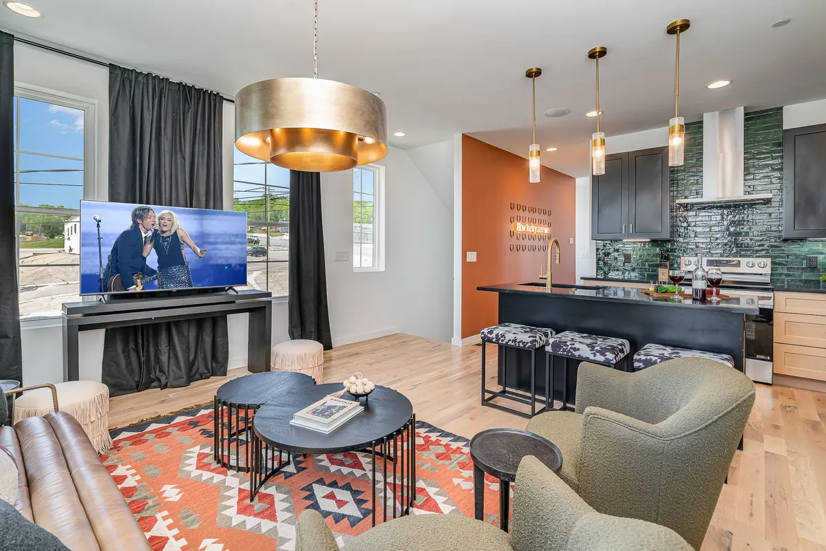 An open-concept living space featuring a plush sofa, coffee table, modern television, kitchen island, and atmospheric lighting. The room is styled for both casual gatherings and more festive celebrations, with a seamless flow between lounging and dining areas.
