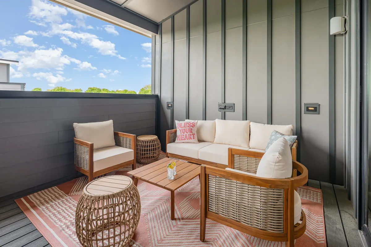 An outdoor seating area with a cozy sofa, woven chairs, decorative pillows, area rug, and coffee table. The scene looks perfect for morning coffee, casual chats, or winding down with friends after exploring the city.